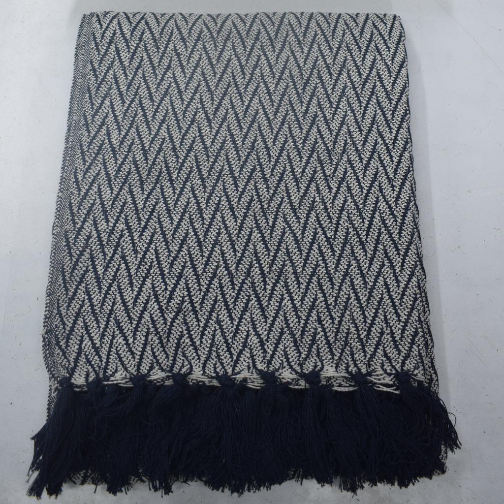A woven throw blanket and matching square pillow set in a gray and white chevron pattern, with the blanket featuring dark navy fringe at the bottom, displayed on a light gray surface.