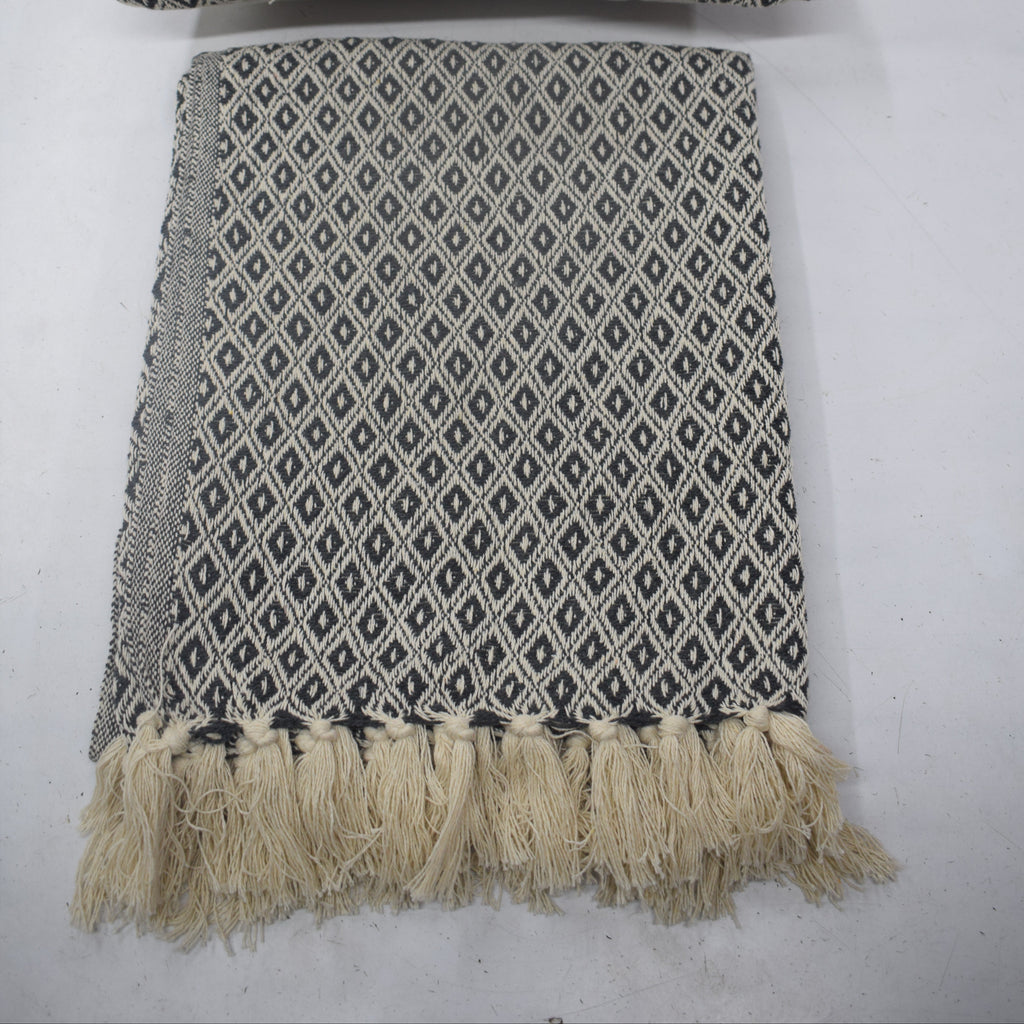 A woven throw blanket and matching pillow set in a gray and white geometric diamond pattern, featuring cream-colored fringe on the blanket, laid flat on a light gray surface.