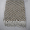 A woven throw blanket and matching pillow set in beige and white with a repeating diamond pattern and fringed edges, laid flat on a light gray surface.