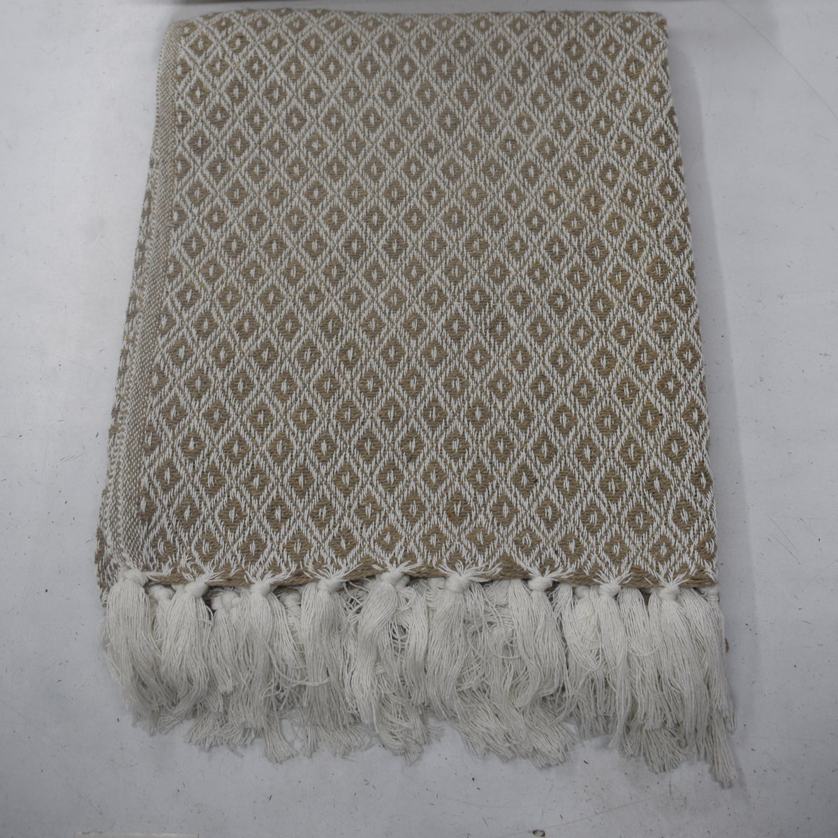 A woven throw blanket and matching pillow set in beige and white with a repeating diamond pattern and fringed edges, laid flat on a light gray surface.